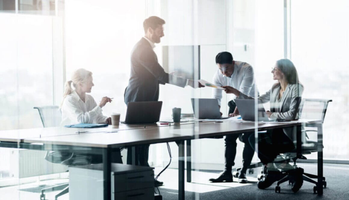 People standing near table, team of young businessmen working and communicating together in office